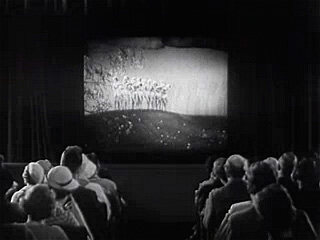 
      Spectators watching a cinema screen in a theatre.
      